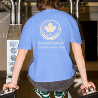 Person wearing a blue t-shirt with a Queens Borough Golf & Recreation logo and text, standing at a security checkpoint.