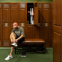 Man sitting on a bench in a locker room with wooden lockers.