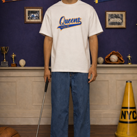 Person wearing a 'Queens Country Club Varsity Script' t-shirt in front of sports-themed decor