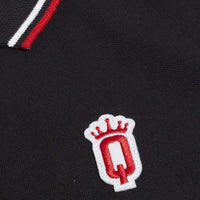 Close-up of red crowned “Q” crest embroidery on black polo shirt