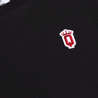 Close-up of embroidered red Q with crown patch on black cotton fabric of QCC T-shirt