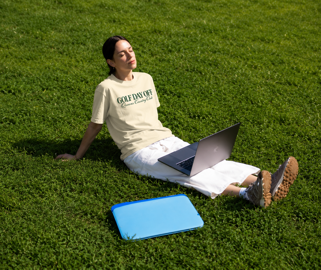 Person sitting on grass with a laptop, wearing a 'Gold Day Off' t-shirt