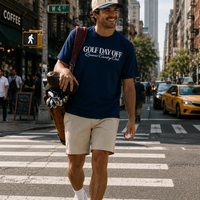 Man walking on a city street wearing a navy blue t-shirt with text and beige shorts.