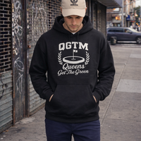 Model wearing black QGTM Queens Country Club hoodie on NYC street, showcasing varsity golf-inspired streetwear design.