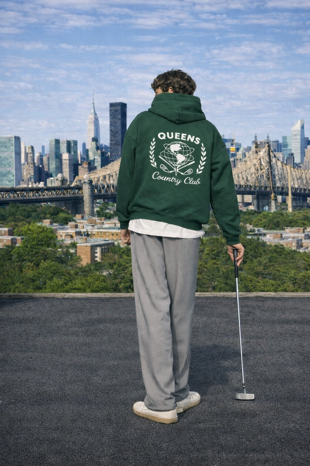   Model with Queens Unisphere Golf Ball Tee Hoodie Forest Green Back looking at NYC skyline on the rooftop in Queens