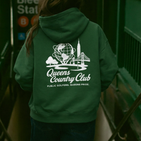 Person wearing a green hoodie with 'Queens Country Club' logo in an urban setting.