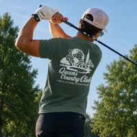 Man golfing on a course with 'Queens Country Club' t-shirt