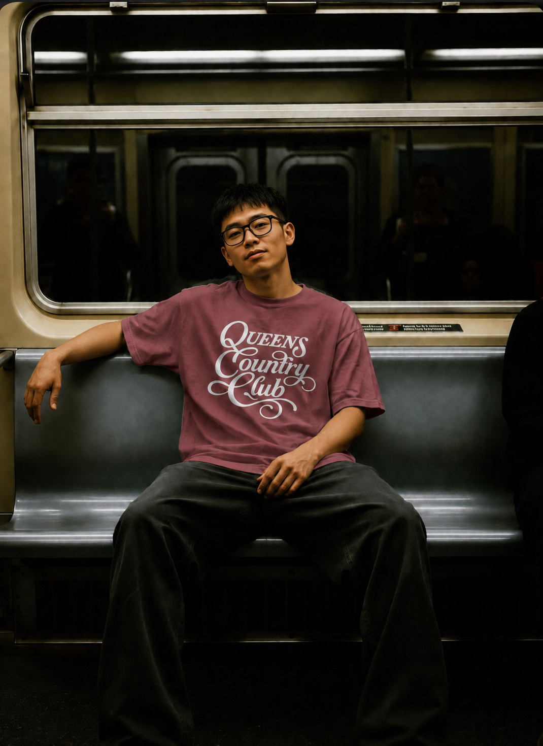 Model wearing a brick QCC Heritage Script heavyweight tee inside a New York City subway car