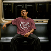 Model wearing a brick QCC Heritage Script heavyweight tee inside a New York City subway car