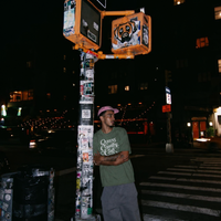 Model wearing a moss QCC Heritage Script heavyweight tee on a New York City street at night