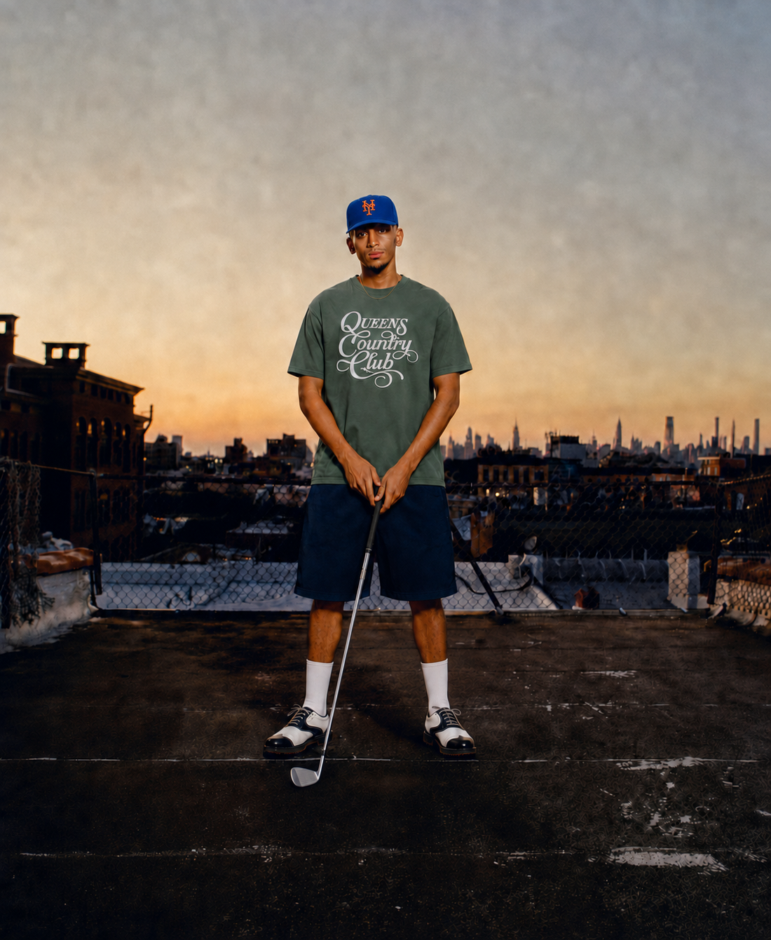 Golfer wearing a moss QCC Heritage Script heavyweight tee on a Queens rooftop at sunset
