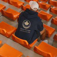 Person wearing a hoodie with a queens borough golf & recreation logo sitting among orange chairs in sports stadium